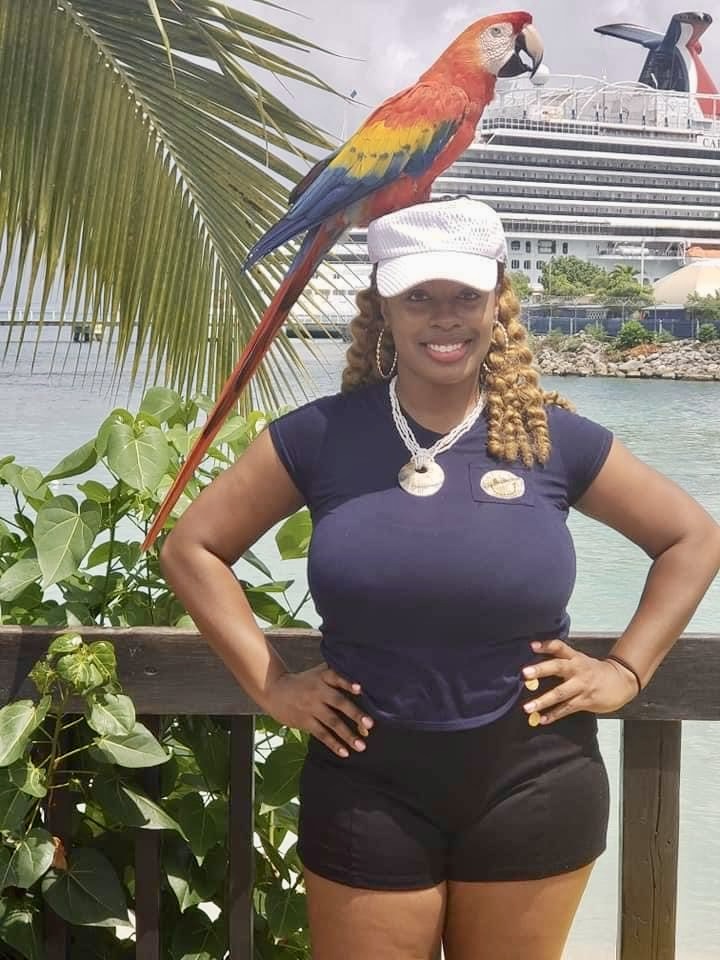 Tamekia Strickland smiling with a macaw perched on her head at a tropical harbor